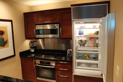 Kitchen area in hotel suite with stove, microwave, refrigerator, and cabinets